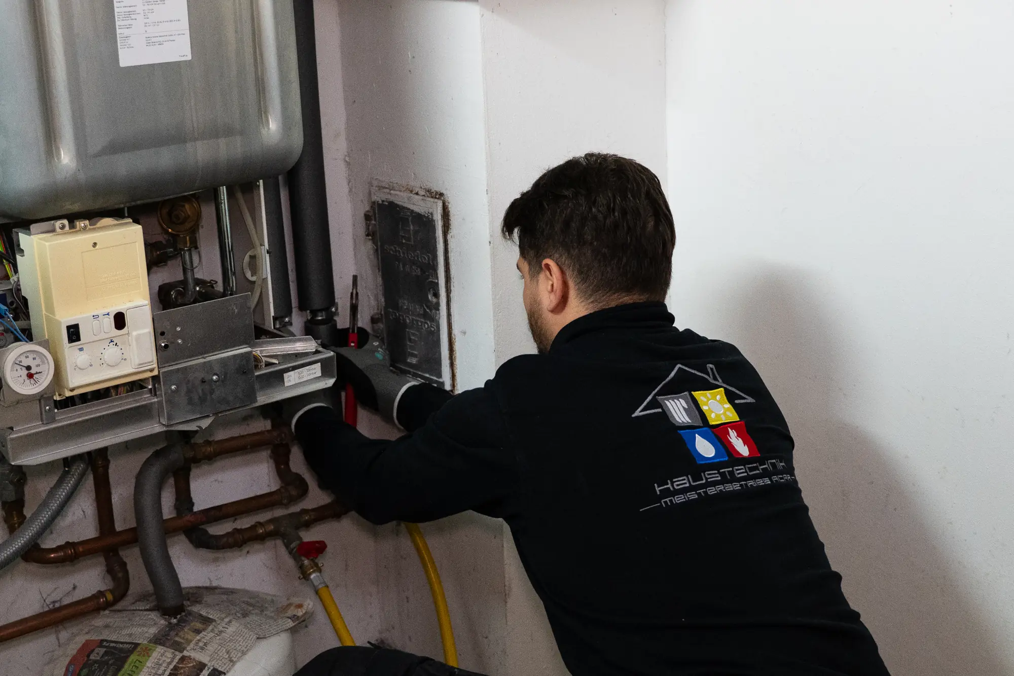 Muhammed Acar mit dem Firmenlogo auf dem Rücken bei der Arbeit an einer Gastherme